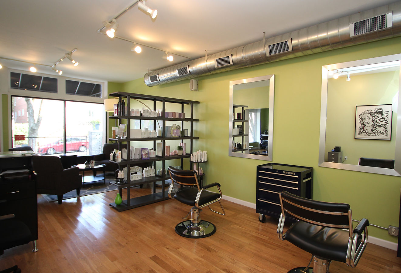 Bright salon floor with green walls, large mirrors, black styling chairs and a shelf of hair products