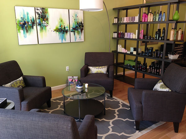 Waiting area with gray armchairs, a glass table, abstract paintings and a product shelf